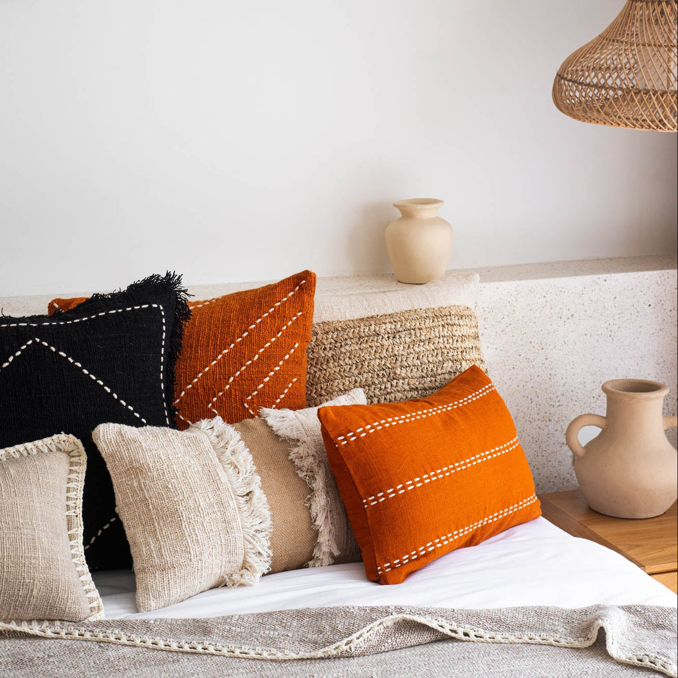 Decorative pillows on a sofa with woven wall art and pendant lamp.