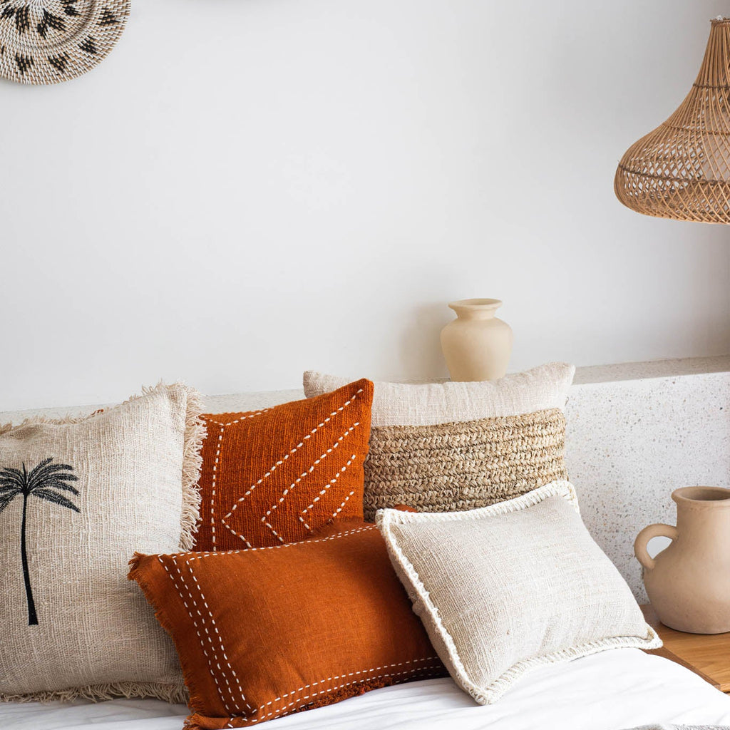 Decorative pillows on a sofa with woven wall art and a vase in the background.