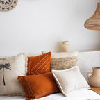 Decorative pillows on a sofa with woven wall art and a vase in the background.