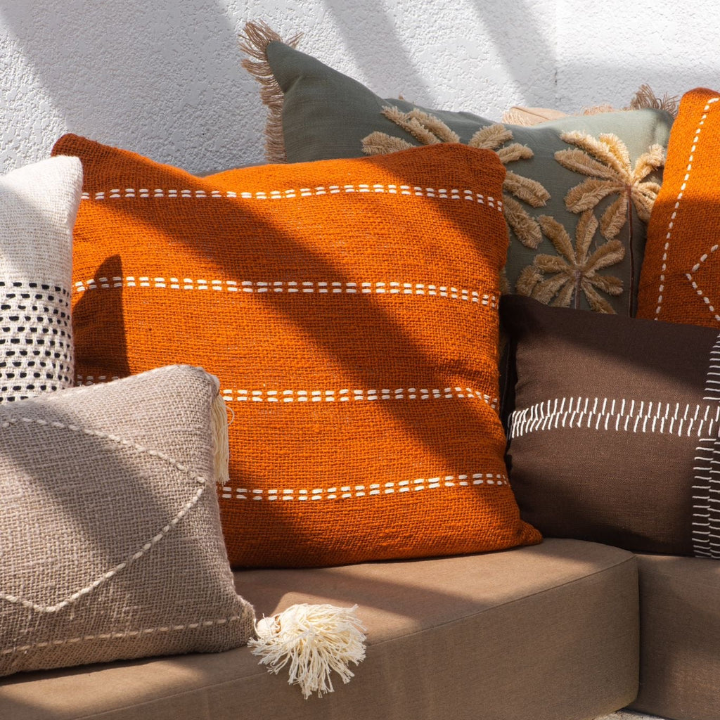 Decorative pillows on a couch with a vase and glass on a table in the foreground.