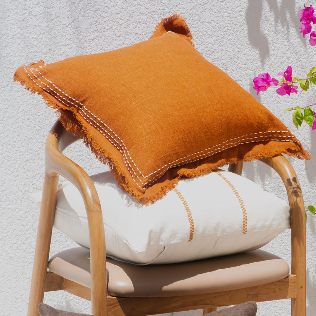 Decorative pillows on a chair with a white wall and pink flowers in the background