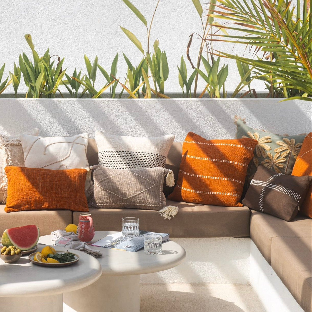Outdoor seating area with a beige sofa, colorful pillows, and a small table with snacks and drinks.