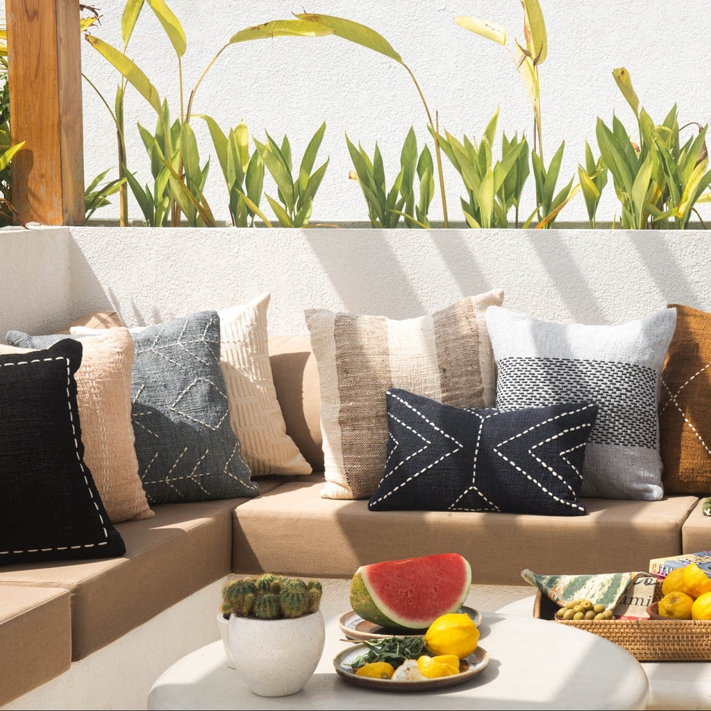 Outdoor seating area with a sofa, cushions, and a small table with fruit and drinks.