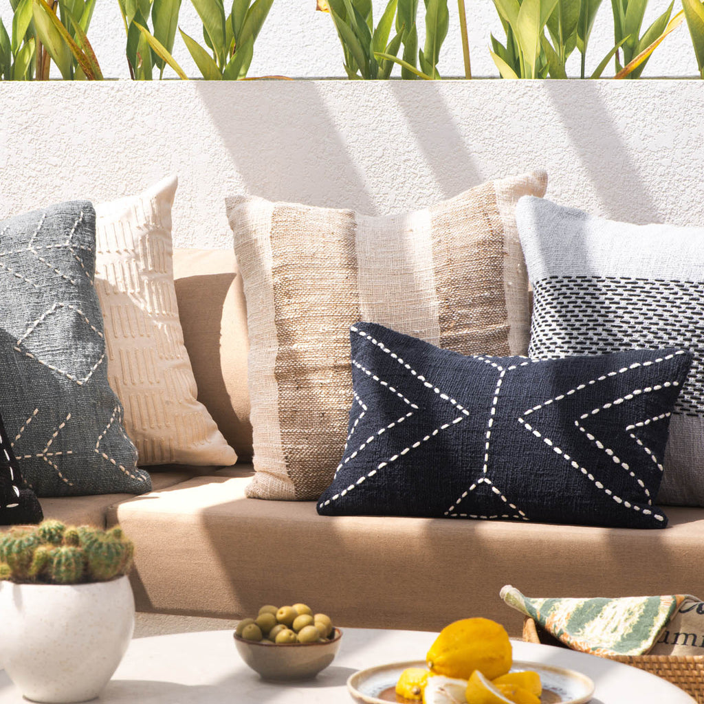 Decorative pillows on a beige outdoor sofa with a coffee table featuring a cactus, bowl of fruit, and plate of food.