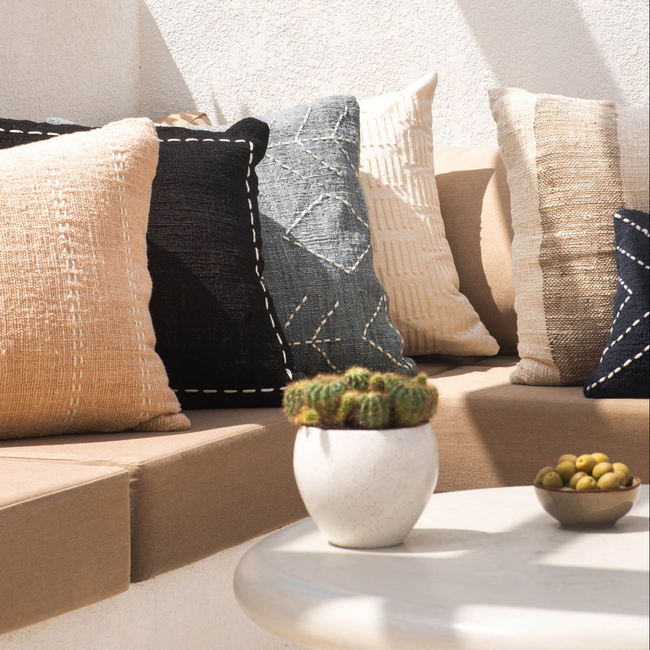 Outdoor setting with a sofa adorned with patterned cushions, a small table with a cactus plant, and a bowl of fruit.