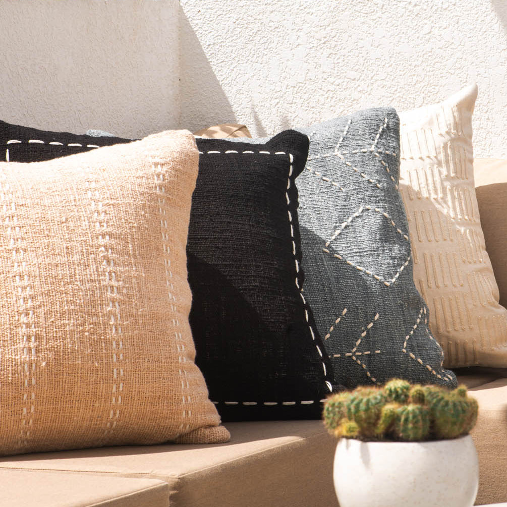 Outdoor setting with a sofa adorned with patterned cushions, a small table with a cactus plant, and a bowl of fruit.