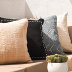 Outdoor setting with a sofa adorned with patterned cushions, a small table with a cactus plant, and a bowl of fruit.