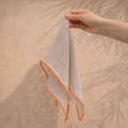 Hand holding a light-colored napkin with orange trim against a beige background