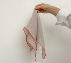 Natural linen napkin with orange hem hanging to show drape and craftsmanship
